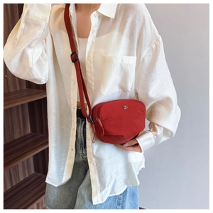 Detail of red fabric crossbody bag with double zippers and silver DD logo on model