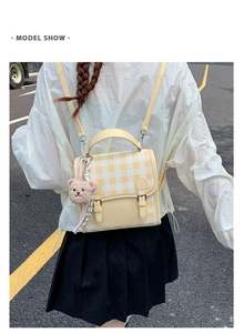 Outdoor back view of a yellow checkered backpack featuring a cute brown plush bear charm