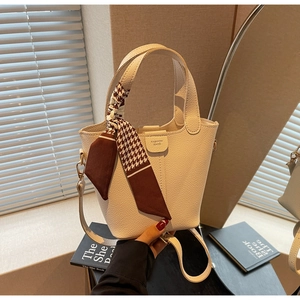 Close-up of cream leather bucket bag with houndstooth silk scarf and gold lettering