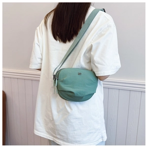 Close-up of a mint green fabric crossbody bag featuring a silver metal D-shaped logo