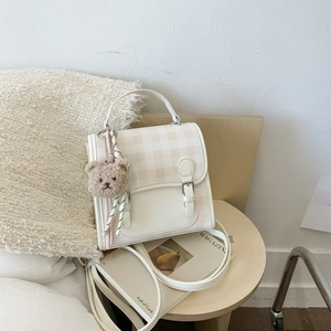 Detail view of cream checkered mini bag featuring a cute brown plush bear charm and tassel