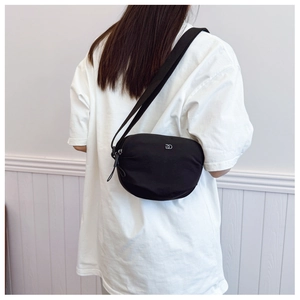 Detail of black crescent crossbody bag with silver metal logo and woven shoulder strap