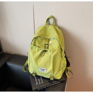 Detail of avocado green nylon backpack with drawstring pocket and brand label on a sofa