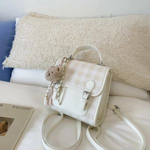 Detail shot of a beige plaid mini backpack featuring a silver buckle and cute bear pendant