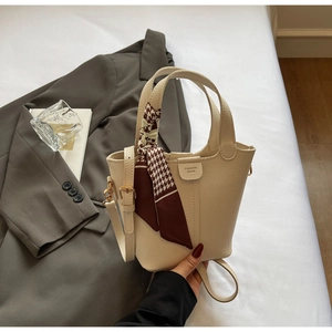 Close-up of beige leather bucket bag with houndstooth silk scarf on white bedding background