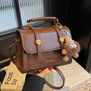 Retro brown crossbody handbag with gold buckles and a cute plush monster charm strap