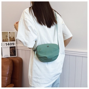 Close-up of sage green shell bag with silver DD logo and adjustable strap