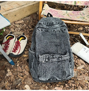 Detail of acid-wash denim backpack showing multi-pocket texture in a camping setting
