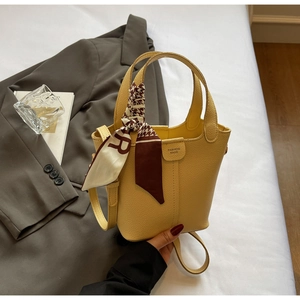 Detailed shot of yellow litchi leather bucket bag with scarf-wrapped handles and long strap
