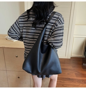 Vista laterale della borsa tote nera in pelle martellata indossata da una modella
