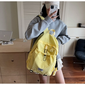 Detail of minimalist yellow nylon backpack showing front drawstring pocket and black carabiner