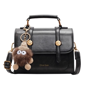 Retro black leather handbag with gold hardware and plush monster charm on white background