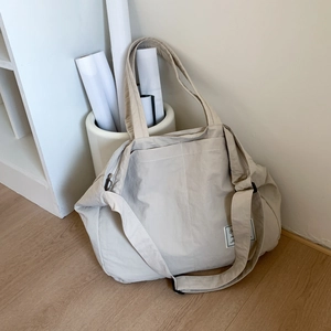 Close-up of beige nylon tote bag featuring adjustable shoulder strap and metal zipper