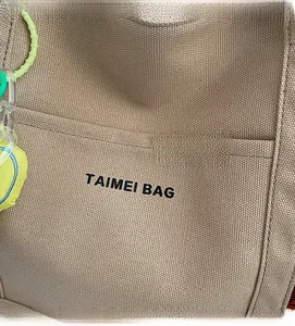 Primo piano della trama del tessuto in tela beige e cuciture con logo TAIMEI BAG