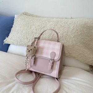 Close-up of pink plaid backpack with dual metal buckles and brown teddy bear charm