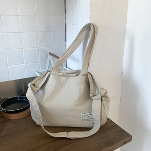 Close-up of beige large canvas tote bag with wide straps and side label on wood desk