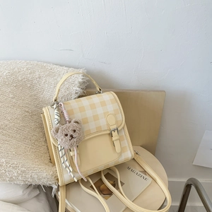 Detail of yellow and white plaid crossbody bag with cute plush bear on a wooden table