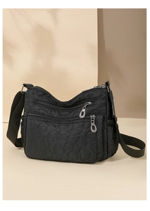 Close-up of black nylon crossbody bag featuring heart quilted texture and silver zippers