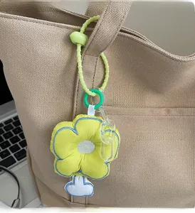 Dettaglio di un ciondolo a fiore giallo con cordino verde su una borsa in tela