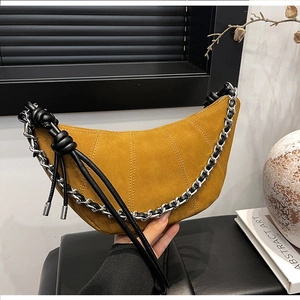 Detail of yellow suede crescent bag featuring pleated stitching and silver chain decor