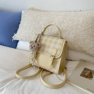 Detail of yellow plaid mini backpack with plush bear charm on a cozy bed background