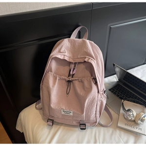 Pink casual backpack featuring drawstring front pocket and woven label in lifestyle setting