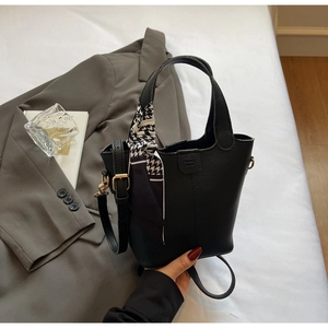 Detailed macro view of black pebbled leather bucket bag with silk scarf on the handle