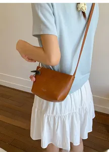 Detailed shot of brown leather crossbody tote featuring a cherry charm and logo