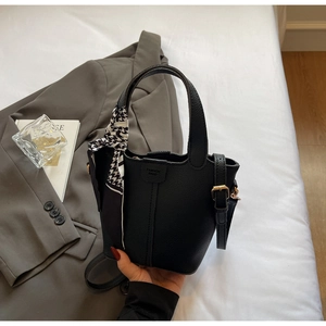 Detail of black pebbled leather bucket bag with a houndstooth scarf and fashion branding