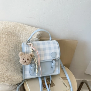 Detail of light blue plaid backpack featuring PU leather texture and a cute bear charm