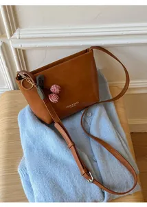 Close-up of brown leather bag with cherry charm on a blue knit cardigan background