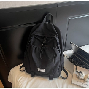 Close-up of black nylon backpack detail featuring white square logo patch and drawstring pocket