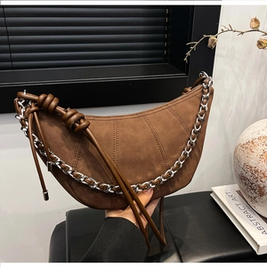 Detail of dark brown suede crescent bag with vertical stitching and silver chain