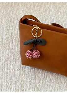 Detailed close-up of brown leather bucket bag with cherry charm on white fabric
