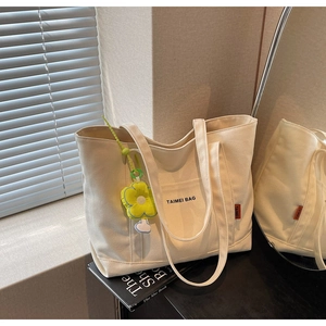 Dettaglio della borsa tote in tela bianco avorio con scritta nera e ciondolo a fiore giallo