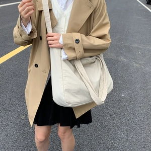 Outdoor street shot of large cream canvas tote bag styled with a khaki trench coat