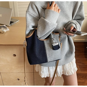Detail of blue denim bucket bag with brown leather trim and mini purse charm