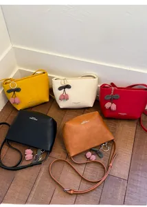 Detail view of five assorted colorful tote bags with cherry charms on a wooden floor