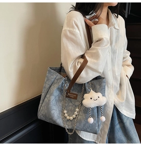 Close-up of light blue patterned denim tote bag with leather straps and charms