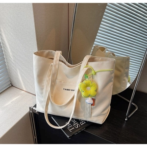 Dettaglio della borsa tote in tela con tasca frontale, ciondolo floreale e luce naturale