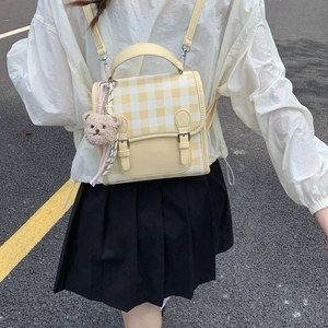 Detail of a yellow and white plaid backpack with metal buckles and a cute plush bear charm