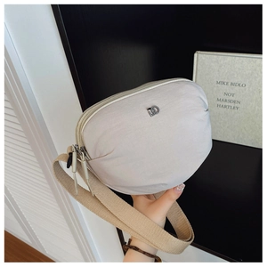 Detail of beige nylon crescent crossbody bag with metal zippers and canvas strap