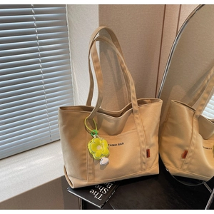Dettaglio della borsa tote in tela beige con tasca frontale e ciondolo a fiore giallo