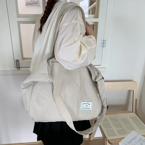 Detail shot of a beige oversized nylon crossbody bag with adjustable wide strap and logo patch