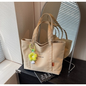 Dettaglio della borsa tote in tela beige con tasca esterna e ciondolo a forma di girasole