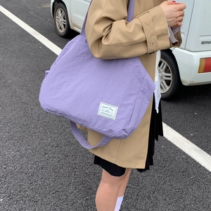 Detail of a large purple canvas tote bag with a white brand label and long shoulder strap