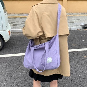 Woman carrying large purple canvas tote bag with wide strap over a tan trench coat