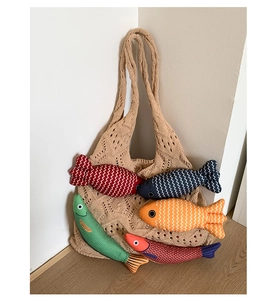 Detail of beige knit tote bag featuring colorful hanging fabric fish charms and hollow design
