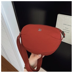 Detail of red semicircular canvas crossbody bag with silver logo and wide shoulder strap