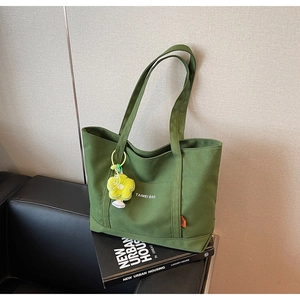 Dettaglio borsa tote in tela verde militare con ciondolo a fiore su divano
